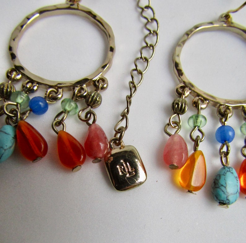 May include: Gold hoop earrings with a dangling charm featuring a variety of colorful beads, including turquoise, orange, pink, and blue. The charm also includes a small gold tag with the letters "RL" engraved on it.