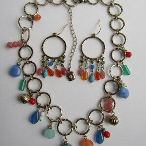 May include: A gold chain necklace with multiple charms, including turquoise, coral, and blue stones. The necklace is paired with matching earrings with similar charms.