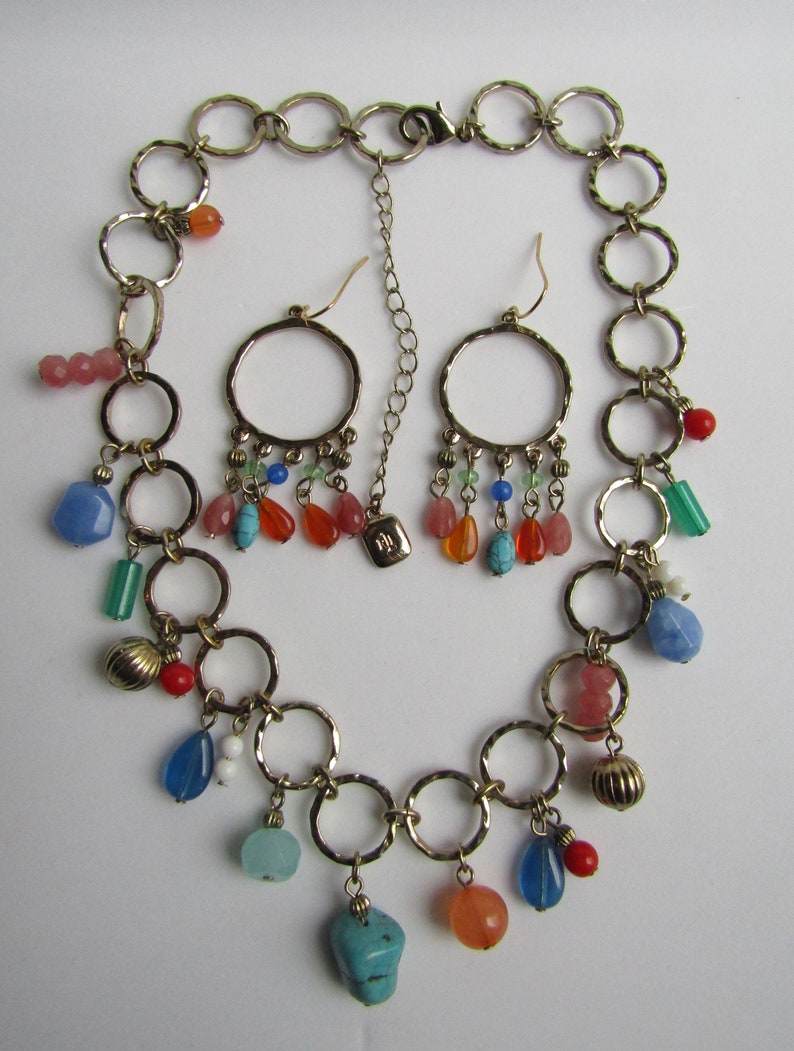 May include: A gold chain necklace with multiple charms, including turquoise, coral, and blue stones. The necklace is paired with matching earrings with similar charms.
