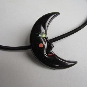 以下が含まれることがあります： 顔を描いた黒い三日月型のヘアゴム。緑色の目と赤い口が描かれている。