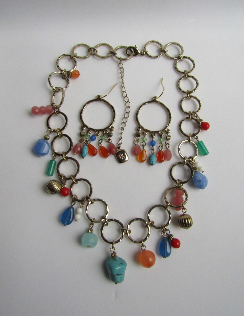 May include: A gold chain necklace with multiple colorful gemstone charms and matching earrings. The necklace features a series of connected rings with dangling charms, including turquoise, red, orange, and blue gemstones.