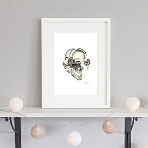 Op de afbeelding: Een zwart-witte tekening van een menselijke schedel met de bovenkant van de schedel verwijderd, waardoor de binnenkant van de schedel zichtbaar wordt. De tekening is ingelijst in een wit frame en hangt aan een witte muur.