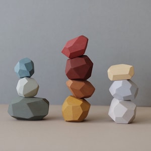 Puede incluir: Un conjunto de formas geométricas de madera de colores apiladas en tres torres. Las torres están hechas de formas geométricas rojas, marrones, amarillas, blancas y azules.