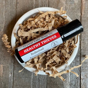 May include: A small glass bottle with a black rollerball top. The bottle is labeled "Healthy Thieves Rollerball Aromatherapy" and "Crystal Lake Soap Co."