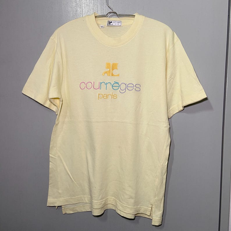 May include: A yellow short-sleeved t-shirt with a multi-coloured embroidered logo that says "Courr&egrave;ges Paris".