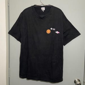 May include: Black t-shirt with a crew neck and short sleeves. The shirt features a small graphic on the upper left chest with the word "sun" and a circular design. The shirt is hanging on a metal hanger.