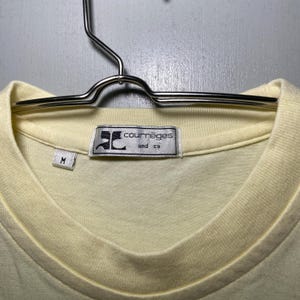 May include: A pale yellow t-shirt with a white tag that reads "Courr&egrave;ges and co" and a size "M" tag.