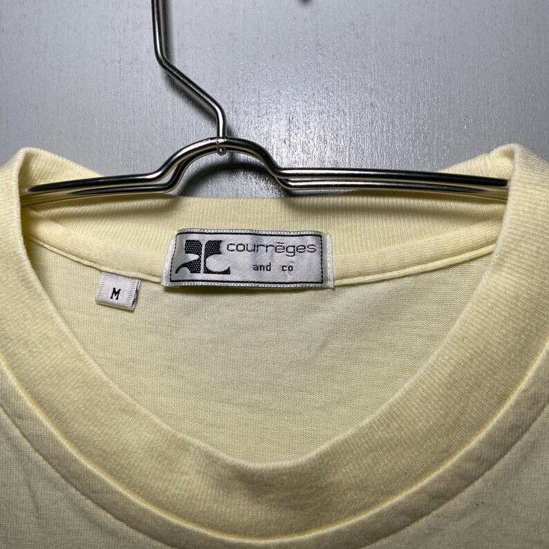 May include: A pale yellow t-shirt with a white tag that reads "Courr&egrave;ges and co" and a size "M" tag.