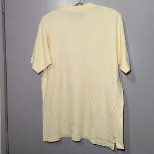 May include: A pale yellow short-sleeved t-shirt with a crew neck.