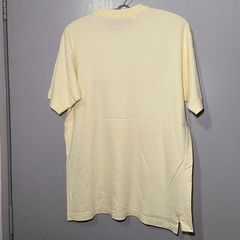 May include: A pale yellow short-sleeved t-shirt with a crew neck.