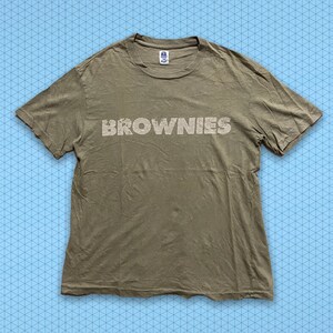 May include: A light brown t-shirt with the word "BROWNIES" printed in white on the front.