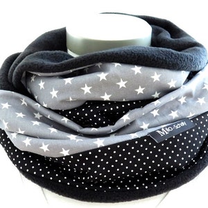 Könnte beinhalten: Ein grauer und schwarzer Infinity-Schal mit einem weißen Sternenmuster und einem schwarzen Tupfenmuster. Der Schal ist mit schwarzem Fleece gefüttert und trägt ein "Milo-Schäby"-Etikett.