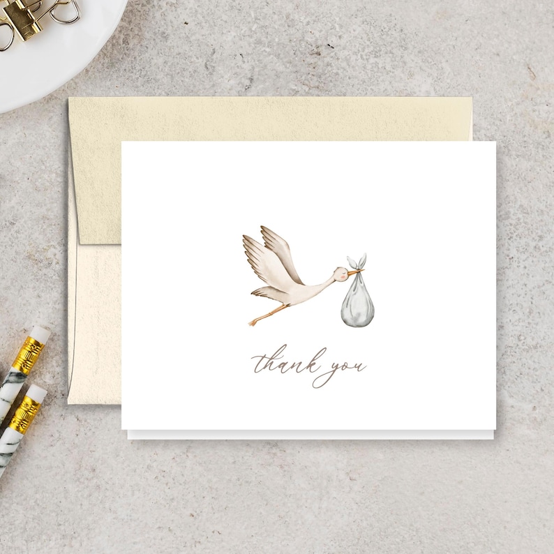 May include: A white card with a watercolor illustration of a stork carrying a bundle. The words "thank you" are written in a delicate script below the image. The card is paired with a cream-colored envelope.