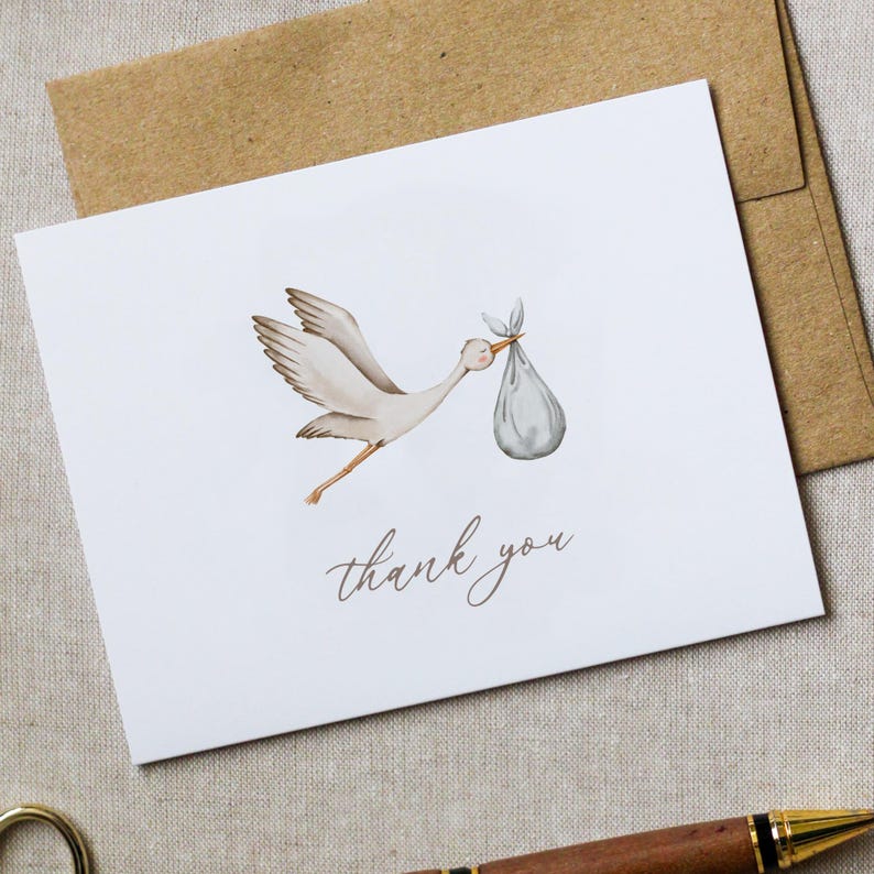 May include: A white card with a watercolor illustration of a stork carrying a bundle. The stork is light brown and gray, with a pink beak. The words "thank you" are written in a delicate script below the illustration. A brown envelope is behind the card.