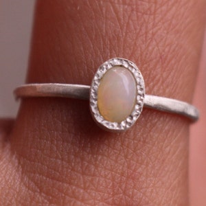 Puede incluir: Anillo de plata con una piedra de &oacute;palo ovalada. El &oacute;palo es de color blanco cremoso con una sutil iridiscencia, engastado en un bisel texturizado. La fina banda pulida le da al anillo un aspecto delicado y elegante.
