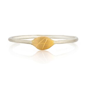Op de afbeelding: Een delicate zilveren ring met een goudkleurig, bladvormig middelpunt. Het gouden gedeelte heeft geëtste lijnen, waardoor een textuurontwerp ontstaat. De ring staat tegen een witte achtergrond, wat de minimalistische stijl benadrukt.