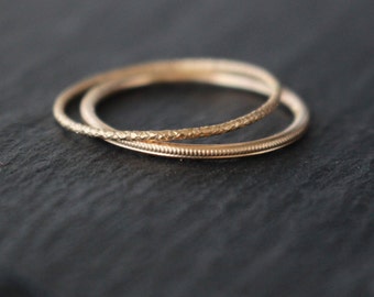 May include: Three gold rings are shown, each with a different texture. One ring has a hammered effect, another has a beaded design. The rings are set against a dark background, which enhances their golden colour and intricate details.