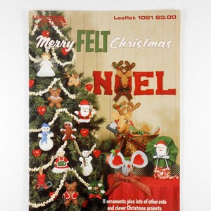 May include: A vintage Christmas craft leaflet titled "Merry Felt Christmas." The cover features a decorated Christmas tree with felt ornaments, including angels, snowmen, and reindeer. The word "NOEL" is prominently displayed.