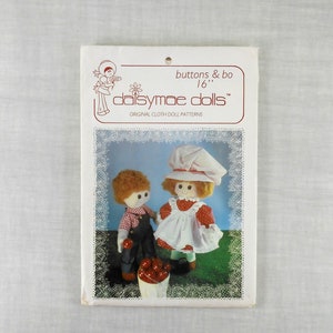 May include: A vintage Daisymae Dolls pattern for making 16-inch cloth dolls. The pattern features a boy and girl doll with red and white accents. The pattern is titled "buttons & bo 16" and "Daisymae Dolls" with the tagline "Original Cloth Doll Patterns".