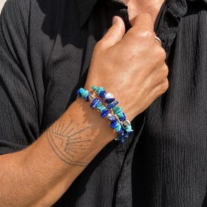 May include: A multi-strand wrap bracelet featuring irregular chip-shaped beads in shades of deep royal blue and bright turquoise, interspersed with small metallic silver-toned accents, creating a layered appearance around the wrist.