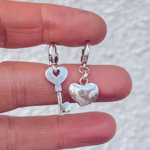 May include: A pair of silver hoop earrings with a key charm and a heart charm.