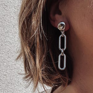 May include: Silver chain earrings with a round, silver charm at the top.