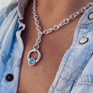 May include: A silver chain necklace with a round pendant featuring a blue gemstone.