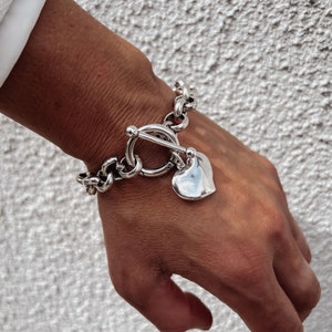 May include: A silver chain bracelet with a heart-shaped charm. The bracelet has a toggle clasp.