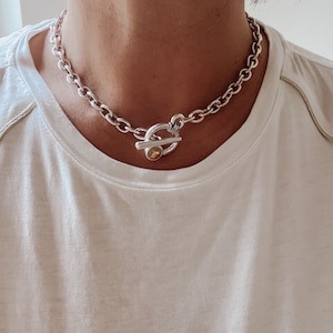 May include: A silver chain necklace with a toggle clasp featuring a round, gold-toned accent.