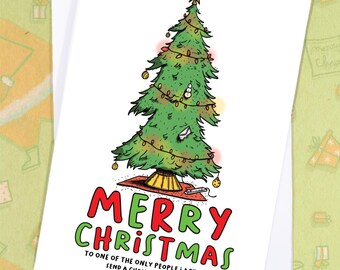 May include: A white Christmas card with a cartoon Christmas tree illustration. The tree is green with gold ornaments and a star on top. The card reads "MERRY CHRISTMAS" in red and green, with a humorous message below.
