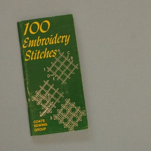 May include: A vintage green booklet titled "100 Embroidery Stitches" with yellow lettering and diagrams. The booklet, from the Coats Sewing Group, features various stitch examples, perfect for embroidery enthusiasts and crafters.