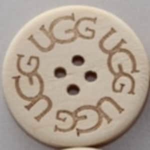 May include: A white wooden button with four holes and the word "UGG" engraved around the edge.