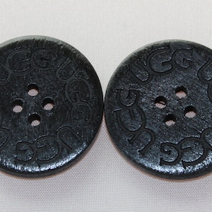 May include: Two black round buttons with four holes each. The buttons have the word "UGG" embossed around the edge.