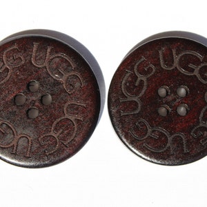 May include: Two brown wooden buttons with four holes each. The buttons have the word "UGG" embossed around the edge.