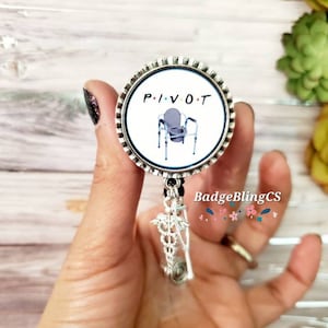 May include: A silver badge reel with a white round charm featuring a cartoon image of a commode chair with wheels and the text "P.I.V.O.T."  The charm is attached to a silver chain with a caduceus charm.