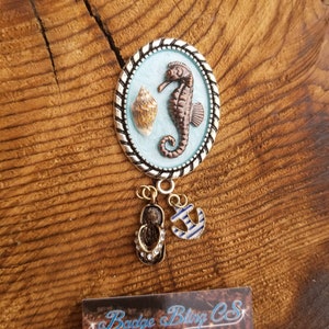 May include: A silver and blue enamel charm with a seahorse and seashell design. The charm has a gold anchor and flip-flop dangle.