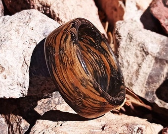 May include: A wooden ring with black and brown wood grain patterns. The ring is made of natural wood and has a smooth, polished finish.