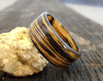 May include: A wooden ring with a black and brown striped pattern. The ring is made of wood and has a natural finish.