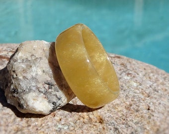Puede incluir: Un anillo de resina dorada con un acabado brillante. El anillo está sobre una roca.