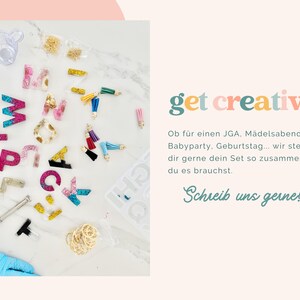 May include: A craft kit featuring resin alphabet letters in various colors and glitter finishes, small colorful tassels, gold-tone hardware, a metal hand drill, and a silicone mold. The text reads get creative and Schrieb uns gerne!