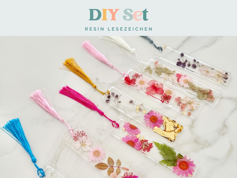 May include: A DIY resin bookmark set. Clear rectangular bookmarks are embedded with dried flowers and gold leaf. Each bookmark has a tassel in pink, yellow, blue, and white. The text "DIY Set RESIN LESEZEICHEN" is at the top.