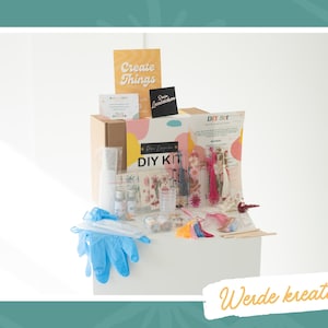 May include: A craft kit containing bottles, gloves, and decorative items. The box is labelled "DIY KIT" and a sign reads "Create Things". The image also includes the text "Werde kreativ!"