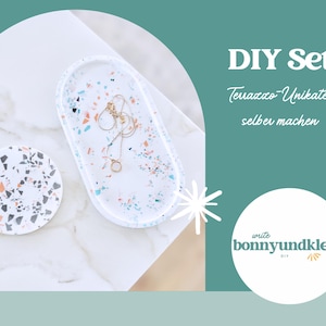May include: A white terrazzo jewelry tray and coaster set with colorful flecks. A gold necklace rests on the oval tray. The image includes the text "DIY Set" and a logo.
