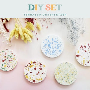 May include: A DIY set of terrazzo coasters in various colors, including red, yellow, green, and blue, with a white base. The coasters are round and feature a speckled design. The text "DIY SET TERRAZZO UNTERSETZER" is at the top.