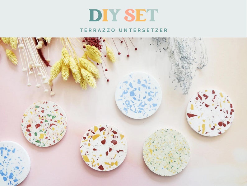 May include: A DIY set of terrazzo coasters in various colors, including red, yellow, green, and blue, with a white base. The coasters are round and feature a speckled design. The text "DIY SET TERRAZZO UNTERSETZER" is at the top.
