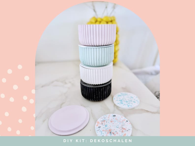 Puede incluir: Una pila de cuatro recipientes cil&iacute;ndricos con texturas acanaladas verticales en rosa pastel, verde menta, blanco y negro. Dos tapas circulares se colocan delante, una de color rosa claro s&oacute;lido y otra con un patr&oacute;n de terrazo moteado multicolor.