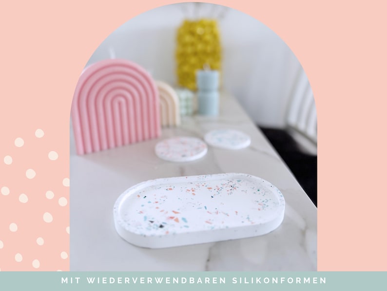 May include: White oval tray with colorful terrazzo-style speckles. A pink rainbow-shaped candle, coasters, and other decorative items are in the background. The text at the bottom reads "MIT WIEDERVERWENDBAREN SILIKONFORMEN".