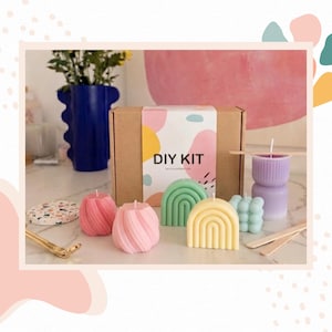 Könnte beinhalten: Ein DIY-Kerzenherstellungsset in einem Pappkarton mit buntem, abstraktem Etikett, umgeben von verschieden geformten Kerzen in Pink, Grün, Gelb und Lila, einem Terrazzo-Untersetzer, einem goldenen Metallwerkzeug und hölzernen Rührstäbchen.