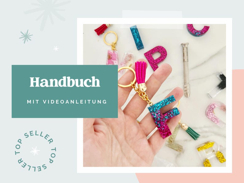 May include: A glittery resin keychain in the shape of the letter F, featuring a gradient of blue and magenta, attached to a gold-tone metal ring with a bright pink tassel. Other resin letter charms and a small metal tool are visible nearby.