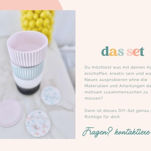 Puede incluir: Una pila de cuatro recipientes cil&iacute;ndricos con texturas acanaladas verticales en rosa pastel, azul claro, blanco y gris oscuro, acompa&ntilde;ados de dos tapas circulares, una rosa s&oacute;lida y una blanca con un patr&oacute;n moteado multicolor.